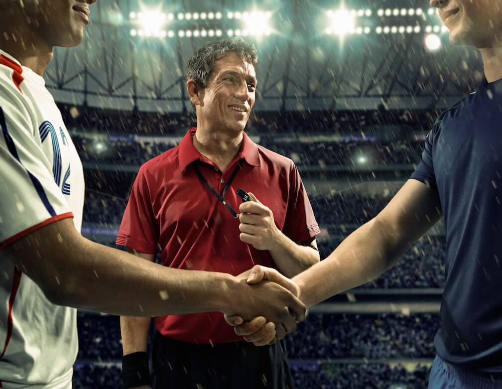 A referee overseeing a prematch handshake before an evenly contested match with evens odds.